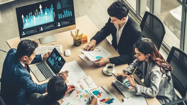 Equipe em reunião analisando gráficos de produtividade em computador, notebook e tablet